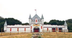 Castle Theatre Reopens at Pleasurewood Hills Castle-style theater building with towers, red doors, and a central sign reading 'Castle Theatre' on a dry lawn.