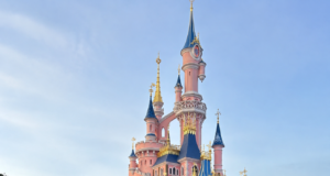 4* Disneyland Paris Hotel Stay, Flights & Optional Park Tickets from Just £89pp Pink fairy-tale castle with blue spires and gold trim atop a rocky hillside against a blue sky.