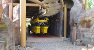 Behind the Scenes Photos of Flight of the Pterosaur at Paultons Park You Need to See Yellow roller coaster train parked on the track inside a rocky, cave-like station area.