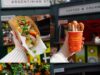 Global Cargo Eats Returns to Alton Towers for Summer 2026 Hand holding a baguette sandwich filled with greens and meat outdoors at a market stall