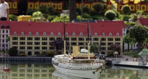 More Than One Million LEGO® Bricks Bring Copenhagen’s Harbour to Life at LEGOLAND® Billund Detailed model ship on calm water with a miniature town featuring red-roofed buildings in the background, reflected in the surface.