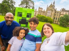What’s Happening at UK Theme Parks This Weekend (18–19 July 2026) Family of four smiling for a selfie on a sunny lawn, with a life-size Minecraft Creeper head behind them and a castle-like building in the background.