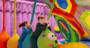 Great Yarmouth Pleasure Beach Opens Brand-New Overplay Family Adventure Today Children ride a large colorful knitted dragon sculpture in a bouncy play area, grabbing green ropes and smiling.