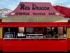 Brand-New Red Dragon Chinese Noodle Bar Opens at Barry Island Pleasure Park Bright red noodle bar stall with a large sign reading 'Red Dragon Chinese Noodle Bar' and workers behind the counter in an amusement park setting.