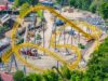 Serpent’s Curse Construction Update: More Track Installed at Paultons Park Aerial view of a yellow roller coaster under construction with scaffolding, dirt ground, and construction vehicles nearby.