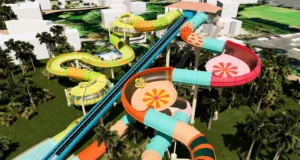 Six Flags Announces Two New Family Water Slides for 2027 at Knott’s Soak City Aerial view of a colorful multi-loop water slide complex among palm trees and white buildings in a tropical park.