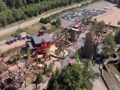 Fireline Redwood Officially Opens at Fraispertuis-City for the Park’s 60th Anniversary Aerial view of a rustic amusement park with red wooden buildings, roller coasters, and a large parking lot nearby.