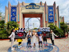 Movie Park Germany Welcomes its 40-millionth Guest Group of people posing with two cartoon clapperboard mascots in front of Movie Park Germany entrance as confetti falls and a roller coaster is visible in the background.