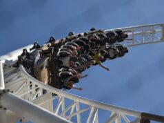 Guests Remember Experiences — Not Ride Specs Riders on a white roller coaster car mid-loop against a bright blue sky, arms outstretched.