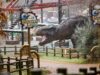 10 Things You Didn’t Know About ROARR! Dinosaur Adventure Huge dinosaur statue in a theme park area with signage reading 'Discovery Land' and a red ride track overhead.