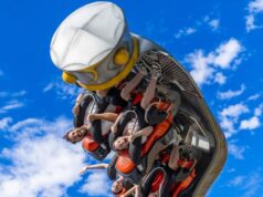 Crealy Theme Park Offers Extreme ROTOR Setting People in a red roller coaster car upside down mid-loop against a bright blue sky, arms raised in excitement.